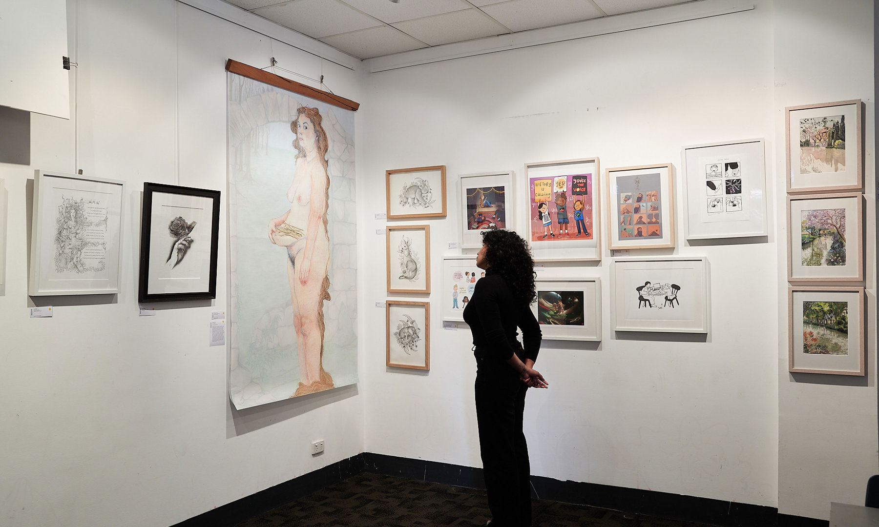 A gallery wall with student illustration artwork displayed. A visitor is viewing an illustration.