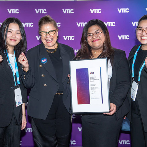 Group of four women in formal suits pose with a certificate in hand.