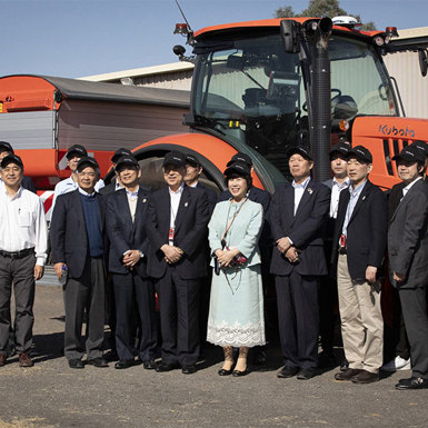 A group of people wearing Kubota caps gathered in front of an orange Kubota tractor.