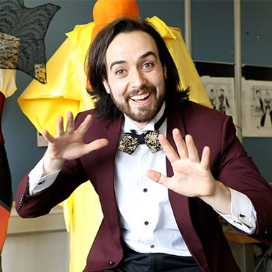 A male theatre student dressed in a suit and bow tie ecstatically smiles at the camera.