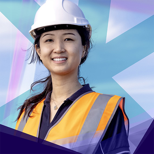 Smiling woman wearing a hardhat and high-visibility safety vest, standing confidently.
