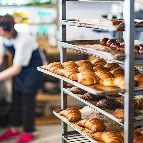 Tray of pastries and croissants on cooling rack with a patisserie student in the background