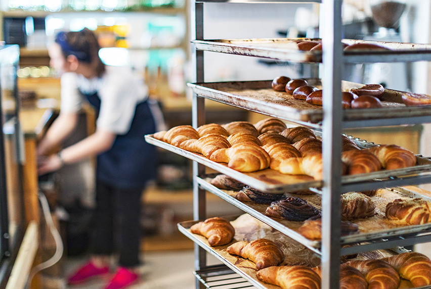 Tray of pastries and croissants on cooling rack with a patisserie student in the background