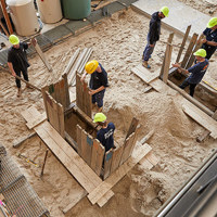 Construction students working in two small trenches, using wooden planks for support.