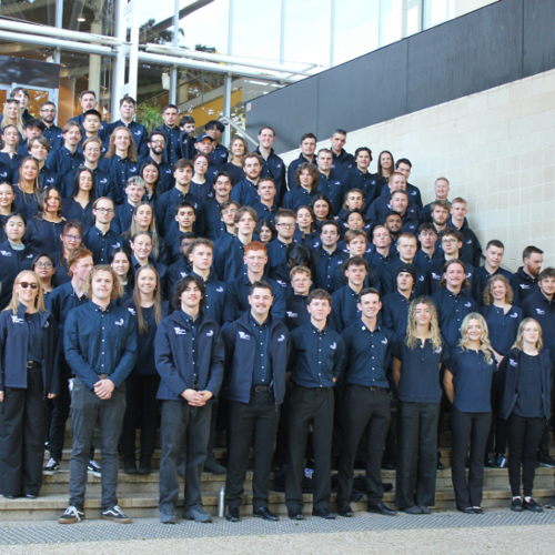 A large group of student competitors on the steps of Brisbane Convention and Exhibition Centre. They are all dressed in a blue WorldSkills uniform with black pants.