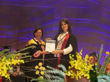 Outstanding student Djuno Fisher and Melbourne Polytechnic CE Frances Coppolillo in graduation regalia. Djuno and Frances are holding their award certificate.