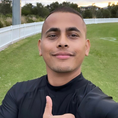 Headshot of Om Guragai on a sports oval, smiling and giving a thumbs-up.
