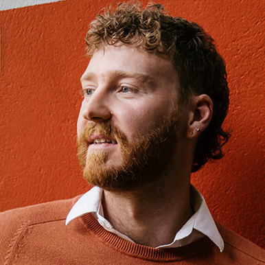 A man with a beard wearing a white shirt and orange sweater