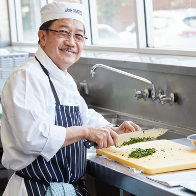 Man in a kitchen wearing a Melbourne Polytechnic kitchen uniform chopping fresh herbs.
