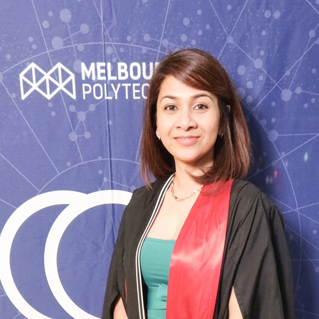 A woman in a graduation gown poses proudly in front of a Melbourne Polytechnic banner, celebrating her academic achievement
