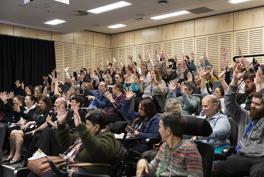 Attendees raising their hands in an auditorium at the Auslan Teachers Conference.