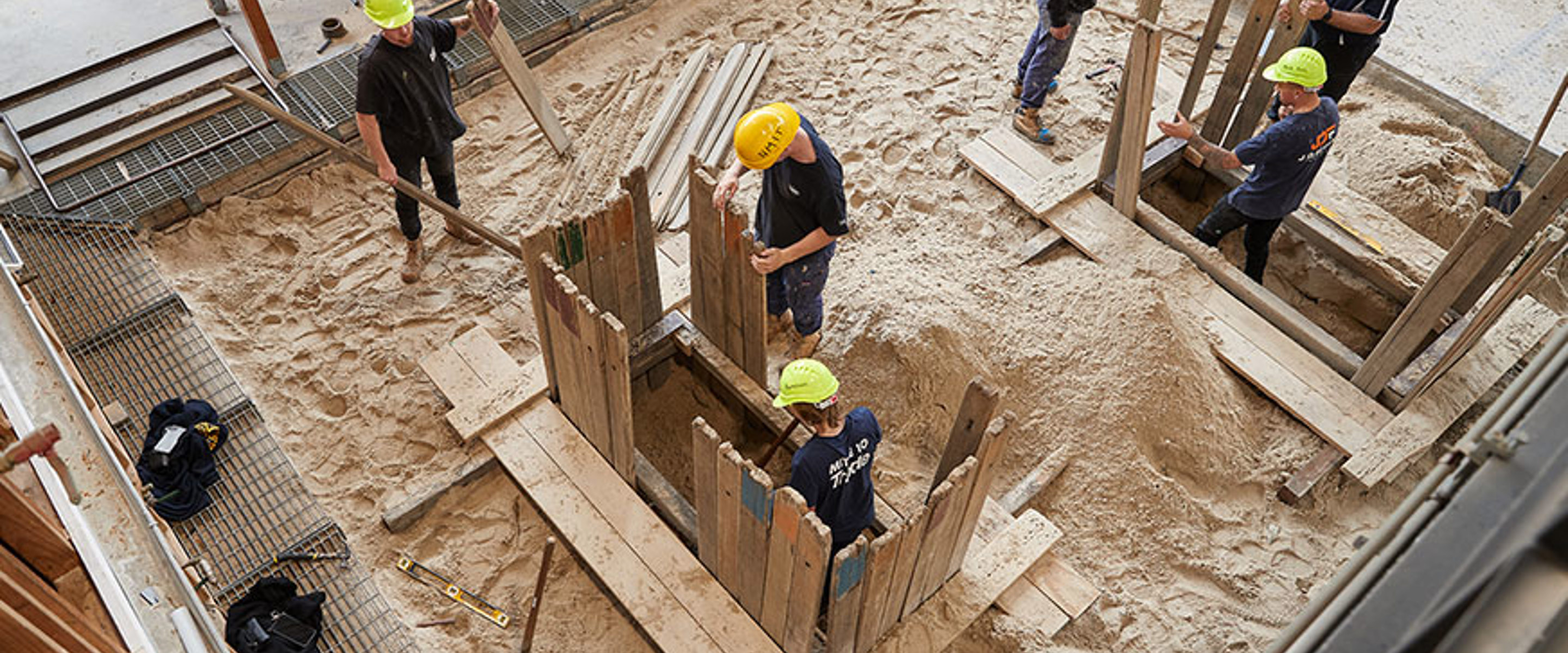 Six plumbing students working on some piping on sandy ground, using tools and equipment to complete the project.
