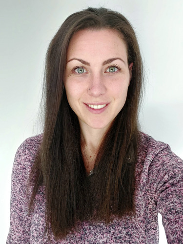 Elisa Gibbs, with long brown hair, wearing a finely knitted pink sweater and smiling.