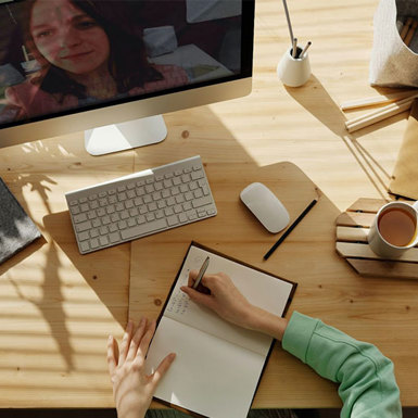 Female student at her desk writing in a notebook while she is in an online tutorial 