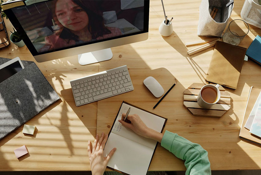 Female student at her desk writing in a notebook while she is in an online tutorial