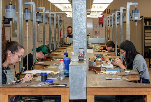 Jewellery students sitting at work benches in jewellery classroom working with tools on competition task
