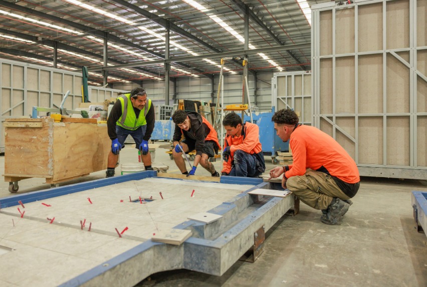 Student apprentices wearing high-visibility shirts focus on a tiling project.