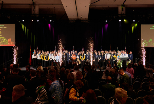 WorldSkills Nationals medal winners standing on stage in auditorium, there are pyrotechnics on the stage and a large audience in the foreground.