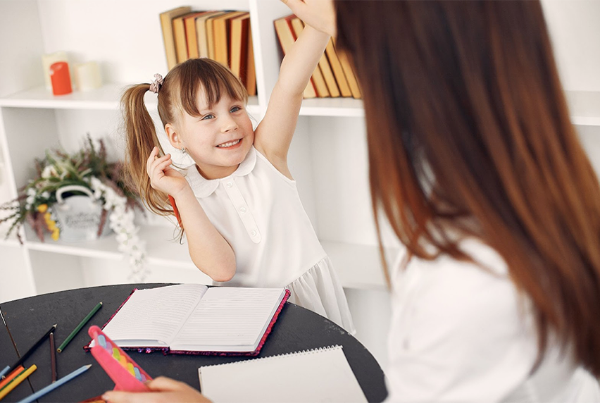 Little girl high-fiving teacher as she completes her homework