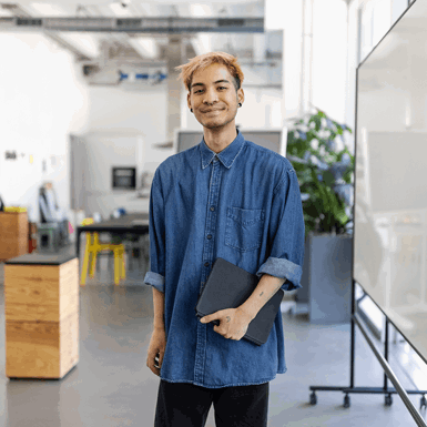Portrait of a young man standing in modern office space holding digital tablet.