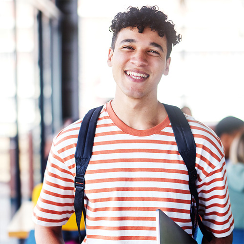 Smiling young man wearing an orange and white striped t-shirt and backpack, with text overlay: '2025 VET Delivered to Secondary Students VDSS'.