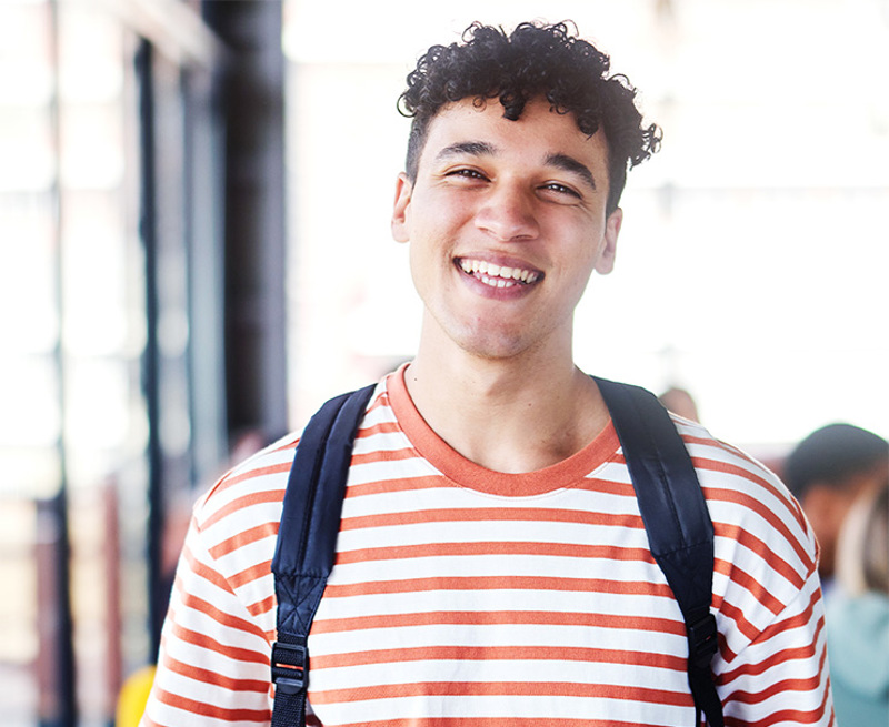 Smiling young man wearing an orange and white striped t-shirt and backpack, with text overlay: '2025 VET Delivered to Secondary Students VDSS'.