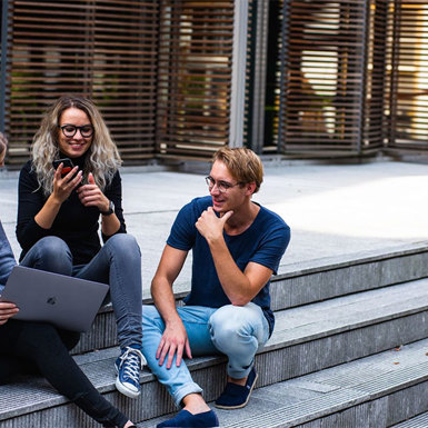 Three students gathered outside by campus steps smiling and talking
