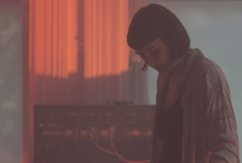 Sara Retallick playing a synthesizer in a softly lit, hazy room.