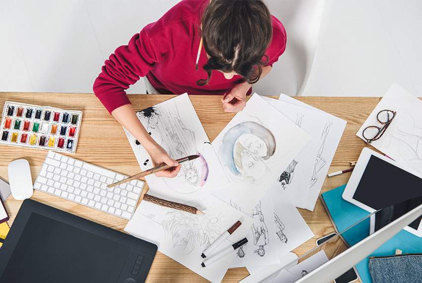 Young girl drawing by table with computer and ipad