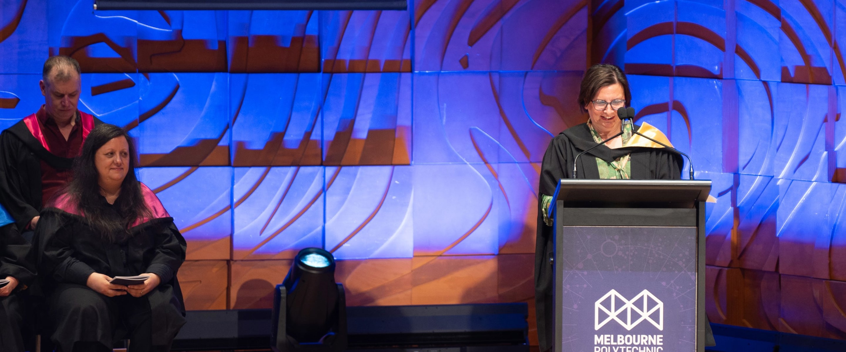 Frances Coppolillo standing at a Melbourne Polytechnic–branded lectern for graduation ceremony.