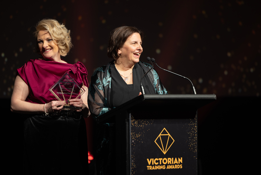 Two women standing at a podium, holding an award, smiling.