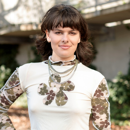 A person wearing a white shirt standing in a garden, smiles at the camera.