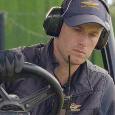 A man in a hat and headphones sits comfortably in a lawnmower cutting the grass