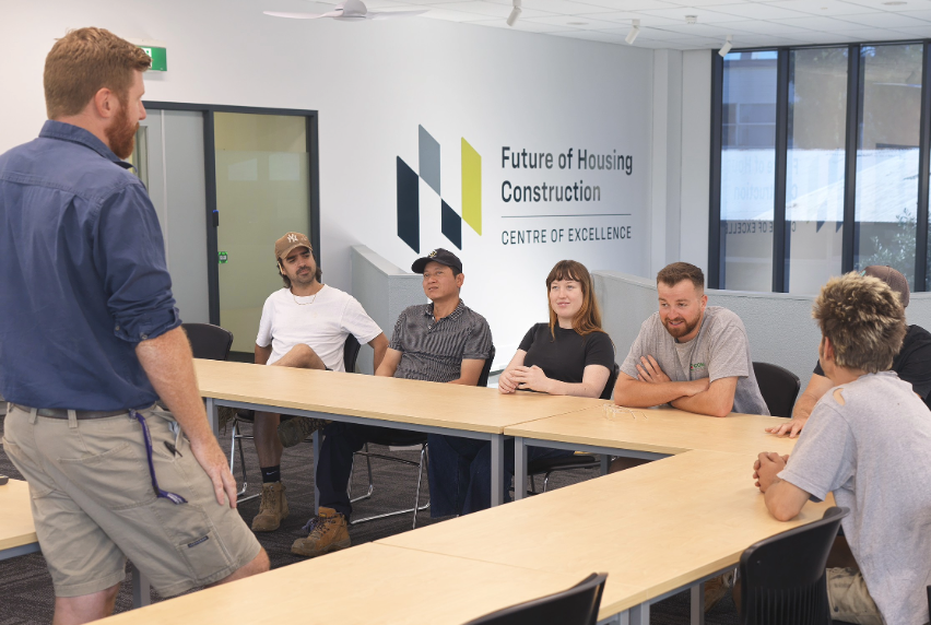 Craig Battams with students at a desk in the Future of Housing Construction Centre of Excellence.